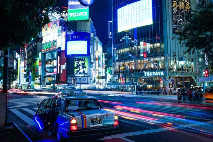 A taxi cab along a busy street in Japan with many LED advertisements visible