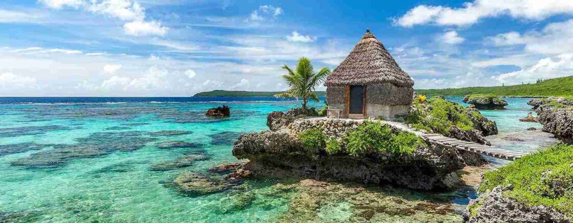 Have it all – tropical escape creative by reborn - reborn - digital creative agency in sydney Traditional island hut on a rocky shore with crystal-clear turquoise water and lush green landscape in the background.
