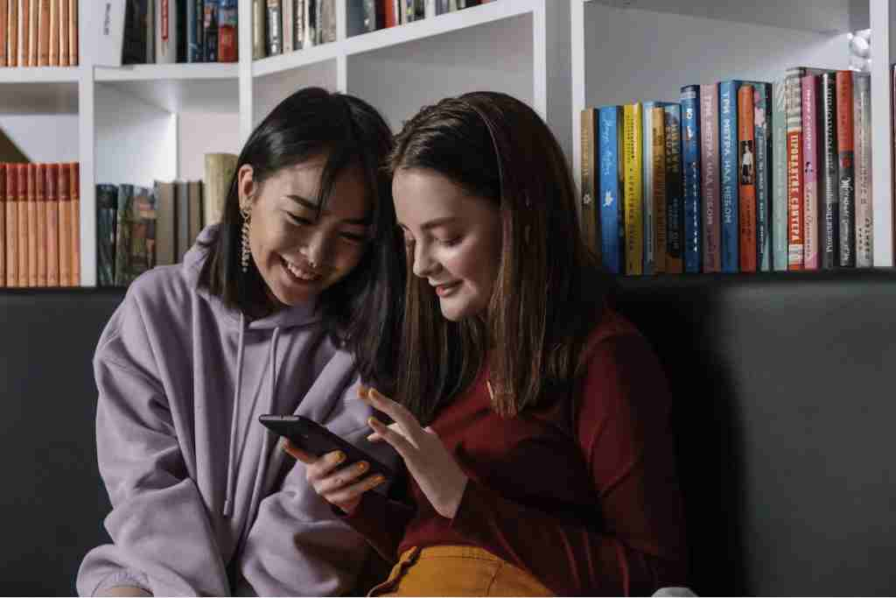 Two young students using a phone in the library