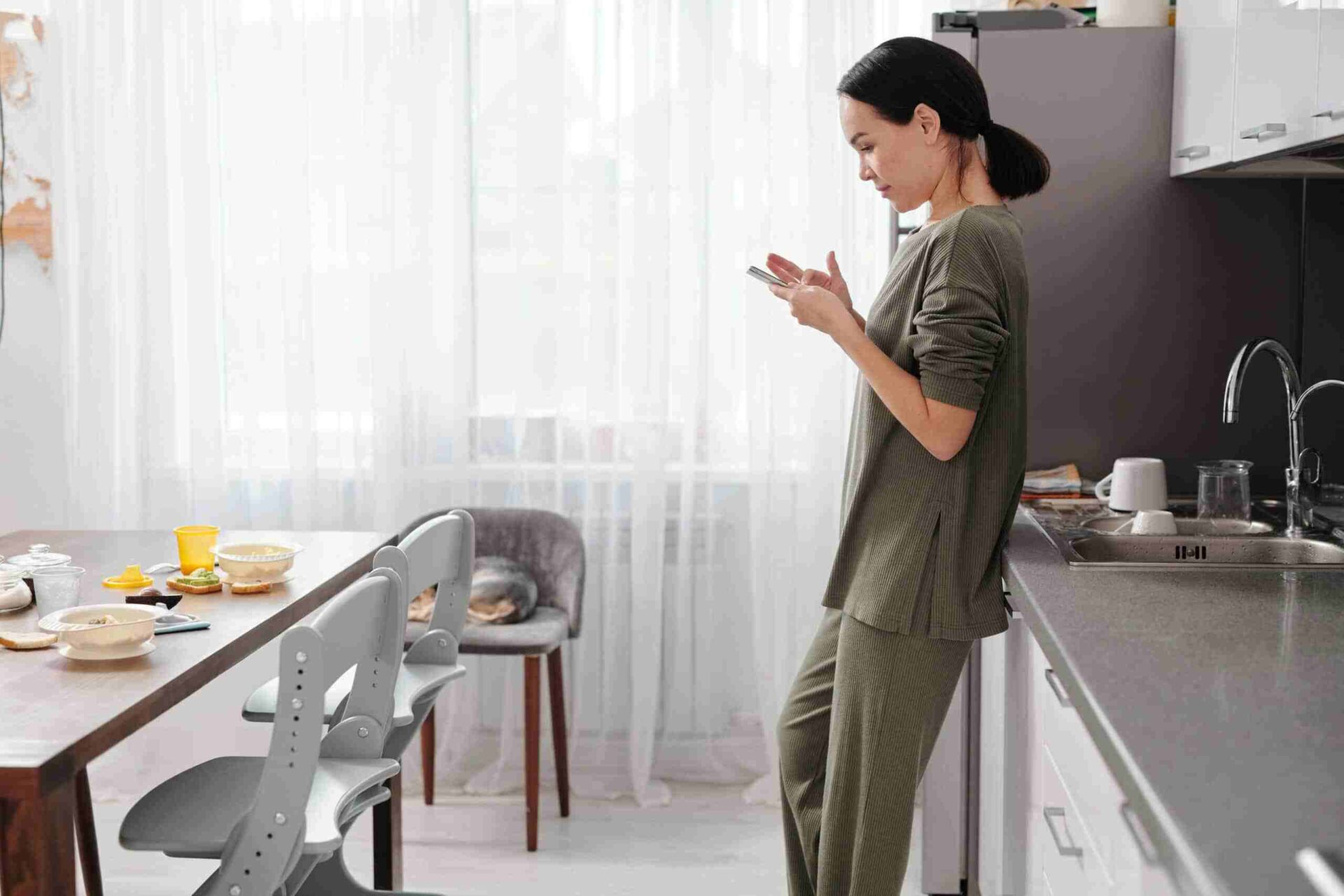 Woman checking her phone in a modern kitchen, representing digital lifestyle and remote engagement by Reborn Digital Marketing Agency.