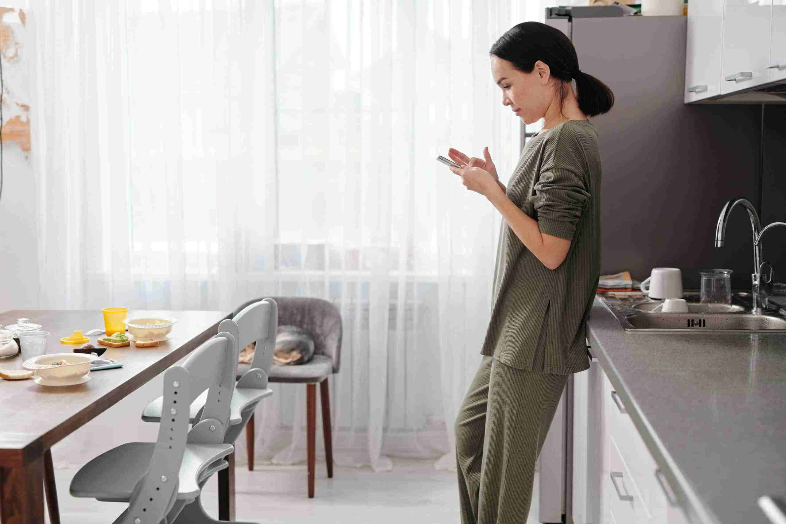 Reborn digital marketing agency – empowering digital lifestyles through mobile engagement - reborn - digital creative agency in sydney Woman checking her phone in a modern kitchen, representing digital lifestyle and remote engagement by Reborn Digital Marketing Agency.